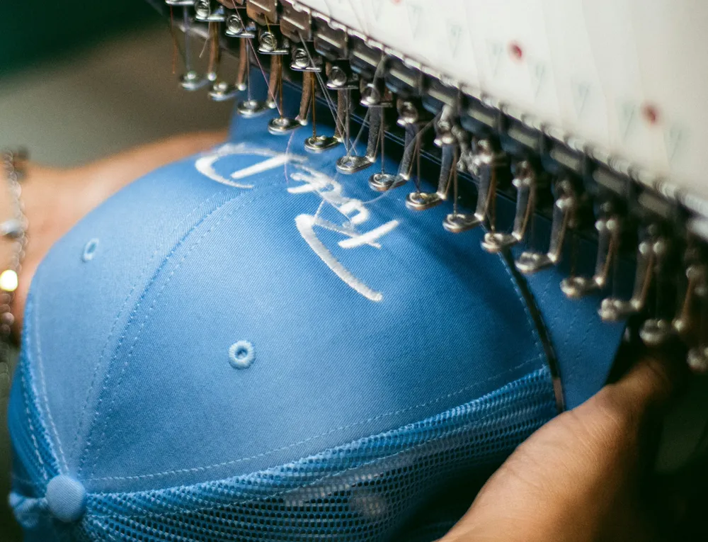 An embroidery machine stitching a logo onto a blue cap